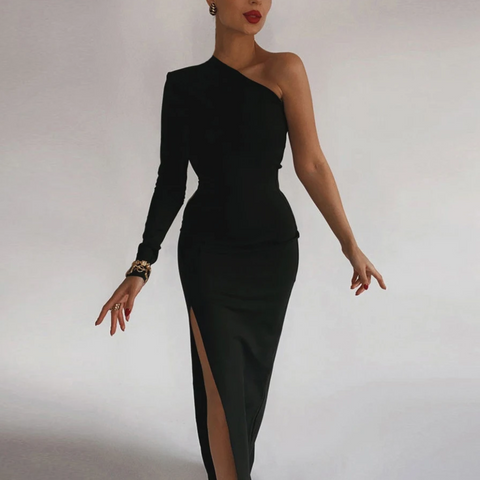 Woman wearing black one-shoulder fitted dress with long left sleeve and high slit, standing against white background with