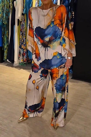 Woman wearing cream-colored outfit with large abstract floral print in navy, orange, and gold. Flowing top and matching