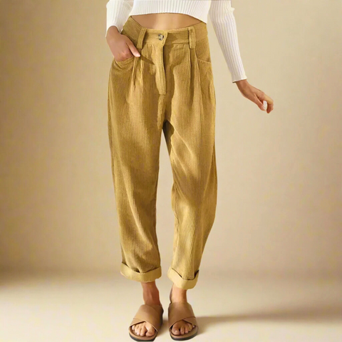 Person wearing golden-yellow corduroy pants with rolled cuffs and a white ribbed long-sleeve top, standing against a neutral