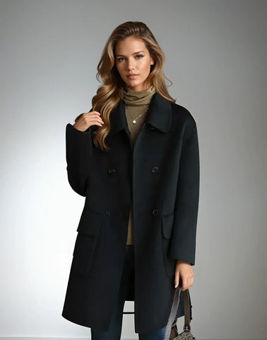 Woman wearing a black double-breasted coat over an olive-green shirt, standing against a light gray background with long