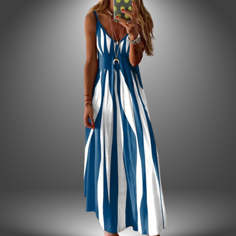 Woman wearing blue and white striped sleeveless midi dress with brown cardigan draped over shoulders, standing against gray