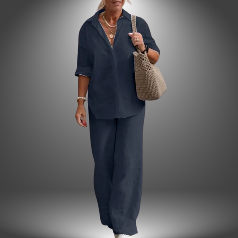 Woman wearing dark navy button-up shirt and matching wide-leg trousers, carrying beige woven shoulder bag, standing against
