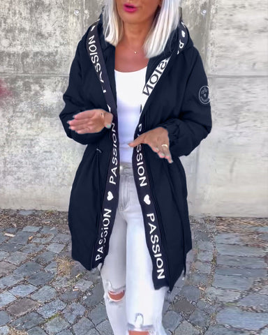 Woman with platinum blonde hair and pink lipstick wearing black hooded cardigan with text on sleeves over white tank top and