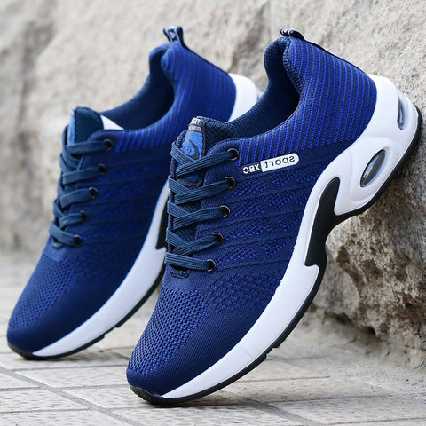 Pair of blue and white mesh athletic sneakers with black accents, displayed on concrete surface against gray textured wall.