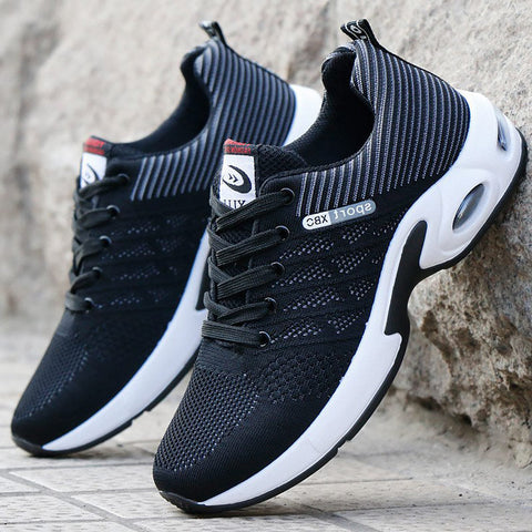 Two black mesh sneakers with white soles and curved white side panels, displayed on concrete surface against a textured gray