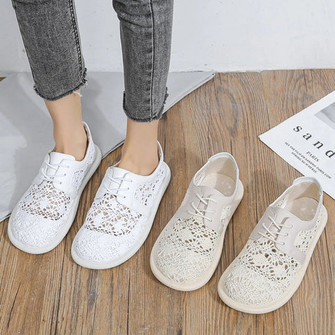 Person wearing gray cropped jeans standing next to two pairs of white lace sneakers on wooden floor, displaying shoe styles