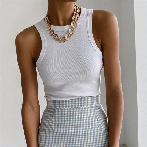 Woman wearing white ribbed sleeveless tank top and gray gingham skirt with gold chain necklace, posed against neutral