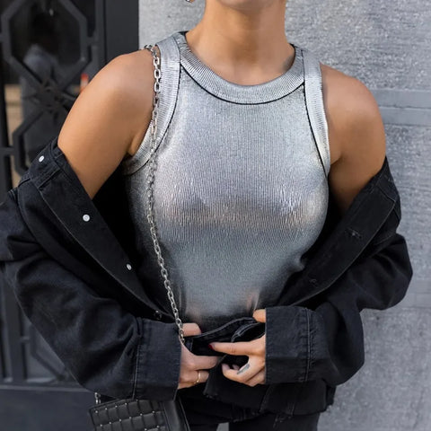 Person wearing gray ribbed sleeveless tank top under black denim jacket, standing against gray textured wall.