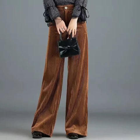 Person wearing rust-colored pleated wide-leg pants, gray cardigan, and holding a black bow-detail clutch against neutral
