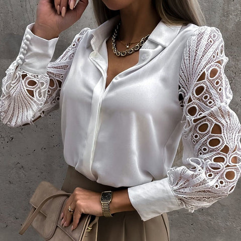 Woman wearing white button-up blouse with intricate lace sleeves, paired with beige skirt and gold chain necklace, against