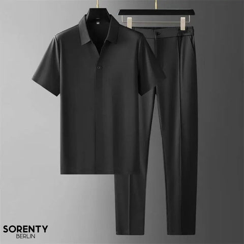 Black short-sleeve button-up shirt and black tapered trousers displayed on hangers against gray background.