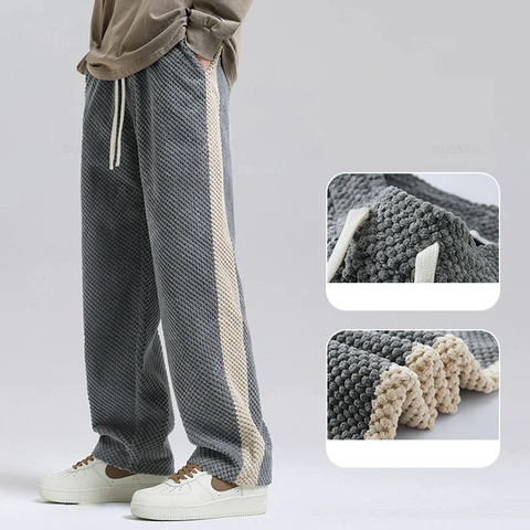 Relaxed-fit knit pants in charcoal gray with cream side stripe, shown on model wearing white slip-on shoes. Textured waffle