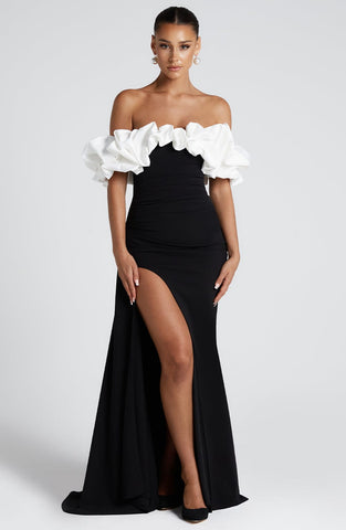 Woman wearing off-shoulder black gown with voluminous white ruffled neckline and high thigh slit, pearl drop earrings