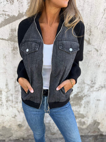 Woman wearing a gray denim vest with black knit sleeves over a white top, paired with blue jeans, standing against a