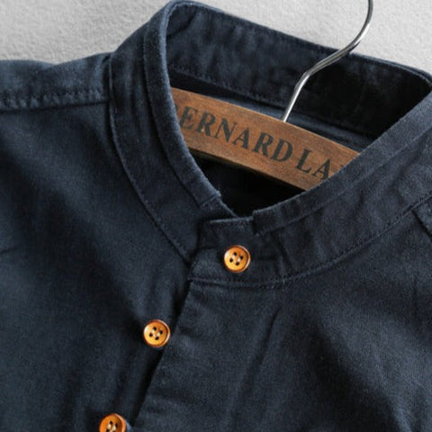 Dark blue denim shirt on wooden hanger, showing collar detail with orange buttons and tan interior label.
