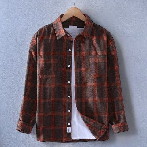 Brown and red plaid flannel shirt on wooden hanger against light blue wall, white buttons visible, white undershirt showing