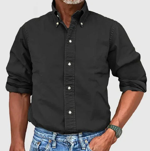 Man wearing black button-up shirt with rolled sleeves and blue jeans, posed against white background.