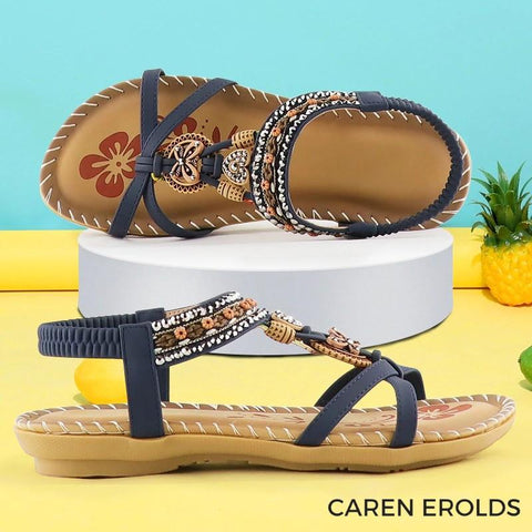 Tan and navy sandals with decorative beading and embroidery on white display podium against turquoise and yellow background