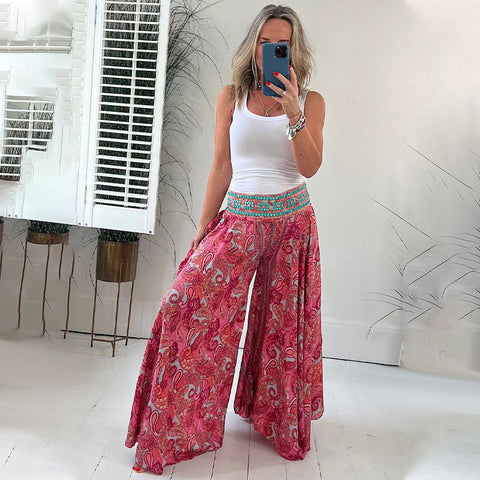 Woman wearing white sleeveless tank top and pink patterned wide-leg pants taking a mirror selfie in bright room with white