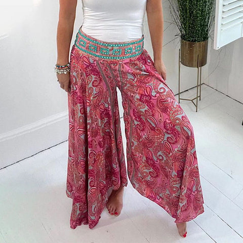 Woman wearing pink paisley harem pants with turquoise patterned waistband, white tank top, standing barefoot in bright white