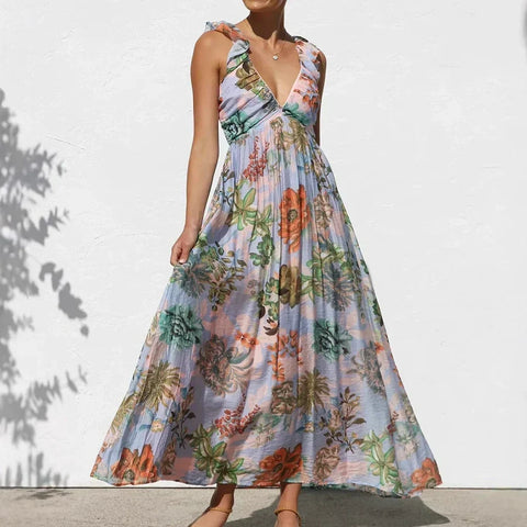 Woman wearing lavender sleeveless V-neck maxi dress with multicolored floral print, standing against white wall with leaf
