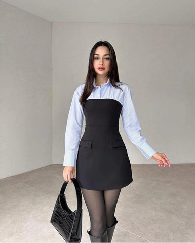 Woman wearing white long-sleeve button-up shirt under black sleeveless A-line dress with front pockets, black tights